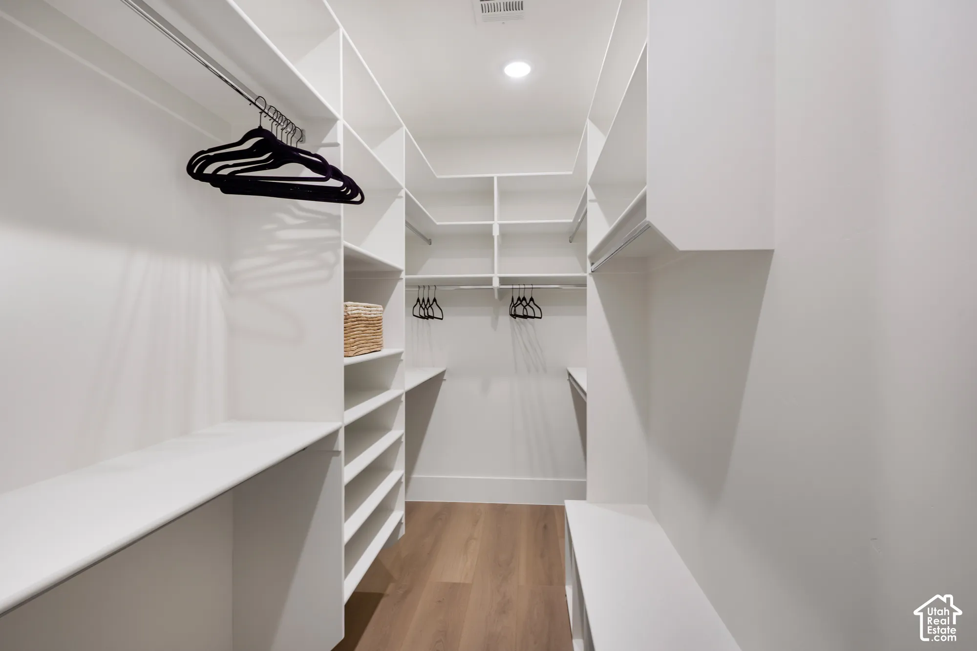 Custom built-in white shelving, multi-level hanging rods, and wood-finish flooring