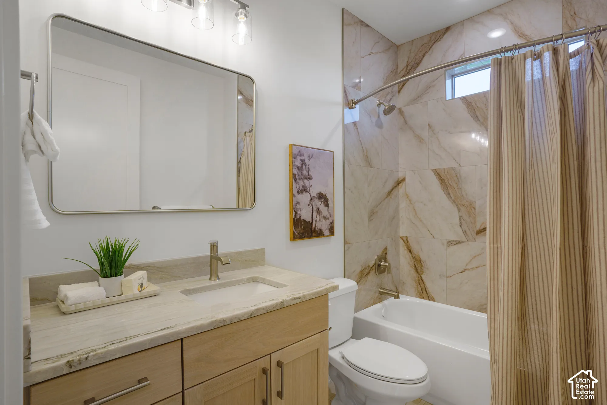 Bathroom featuring a light-toned wood vanity with an integrated stone-finish countertop, a rectangular undermount sink, a polished metal faucet, and a large rectangular mirror