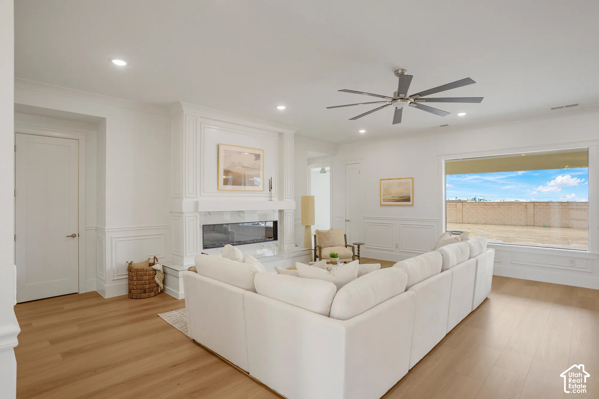 Wood-finish flooring, recessed lighting, ceiling fan, wainscoting, and a linear fireplace with a traditional mantel