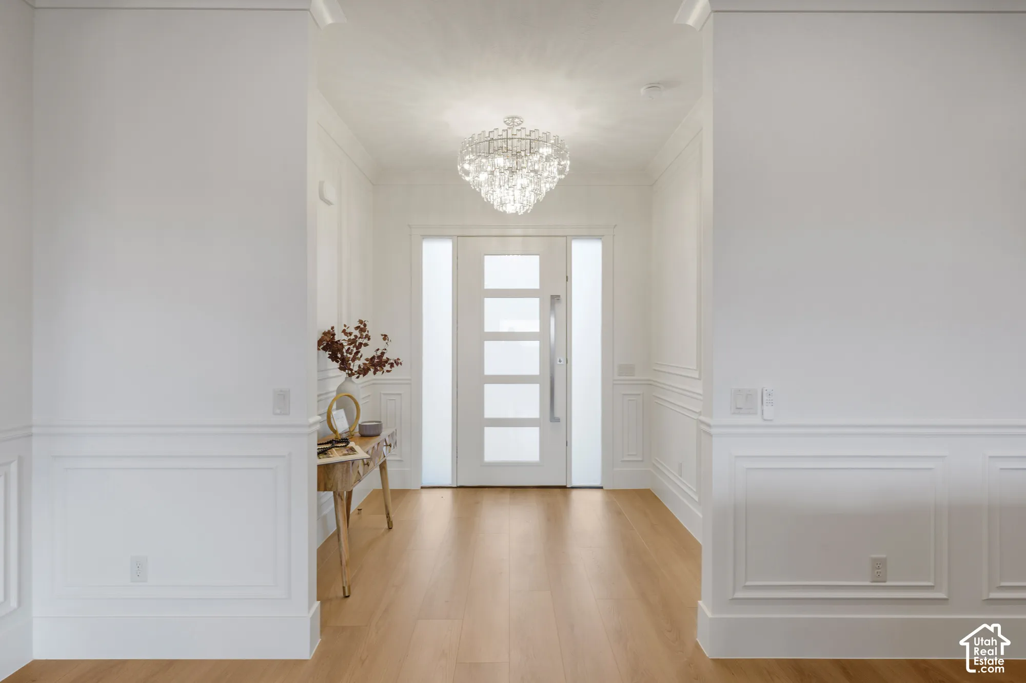 Entryway featuring wood-finish flooring, white wall paneling, a multi-pane glass door with side lights, and a crystal chandelier
