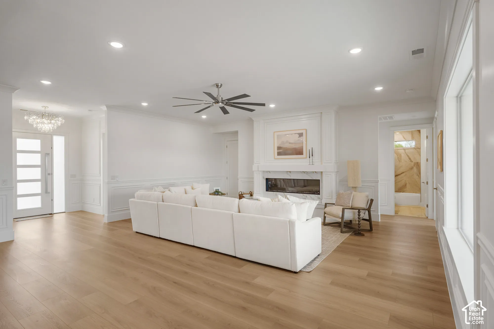 Open-concept area featuring wood-finish flooring, recessed lighting, a modern horizontal fireplace with a custom mantle, wainscoting, and a multi-pane glass entry door