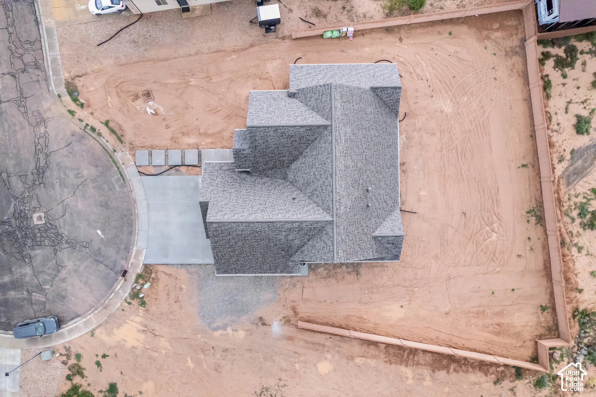 Aerial perspective of property featuring a multi-gable shingle roof, concrete driveway, and expansive corner lot enclosed by perimeter fencing