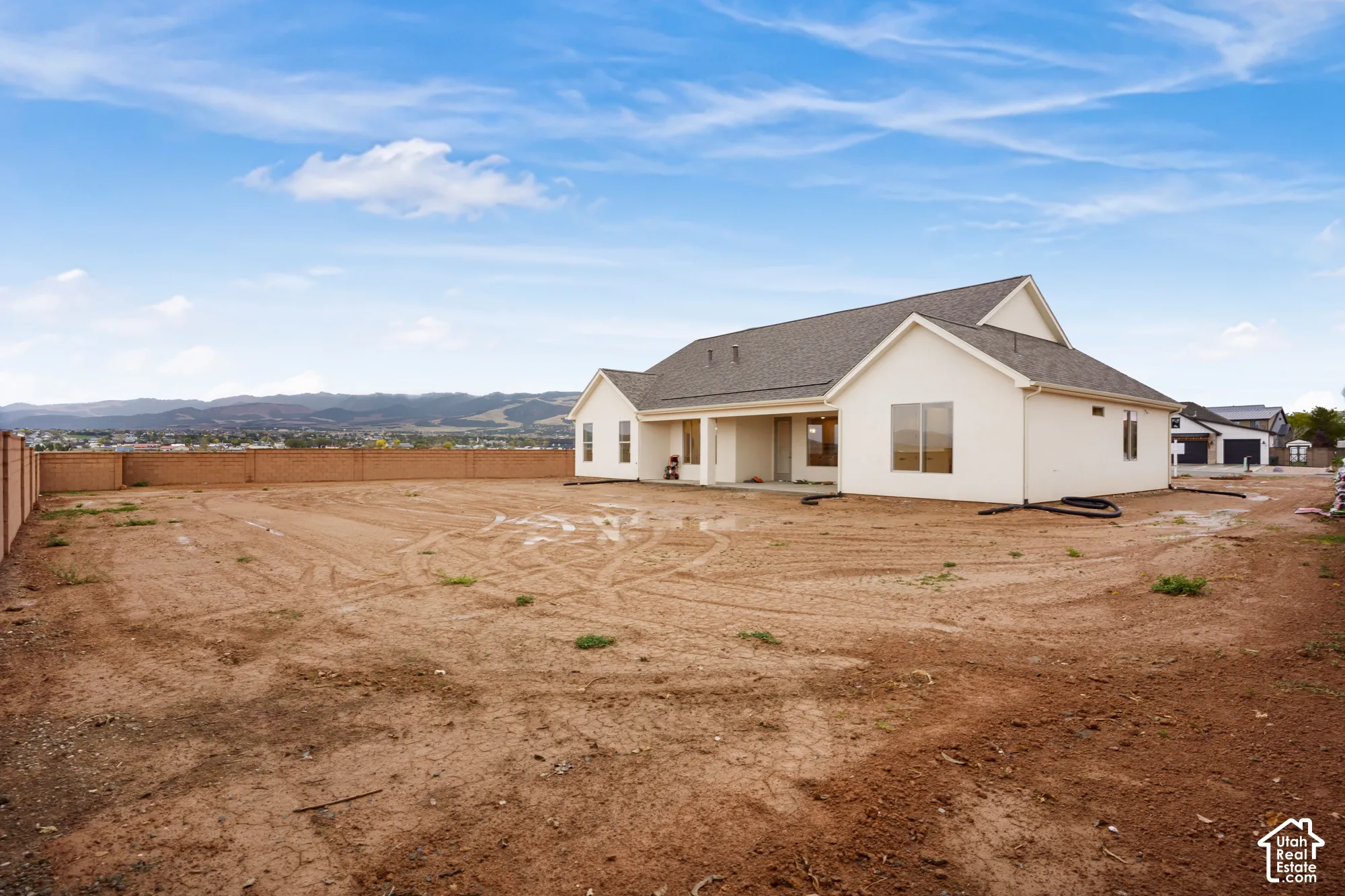 Rear exterior featuring a light-colored stucco facade, pitched asphalt shingle roof, expansive backyard space, perimeter masonry wall, and distant mountain backdrop