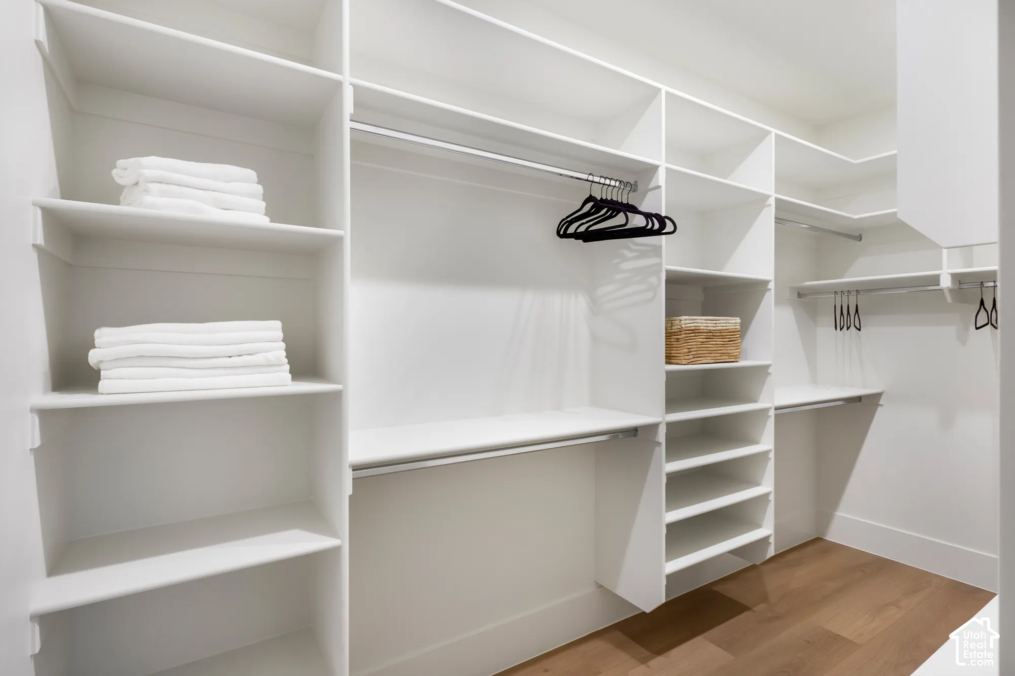 Custom walk-in closet featuring white built-in shelving, multiple hanging rods, and wood-finish flooring