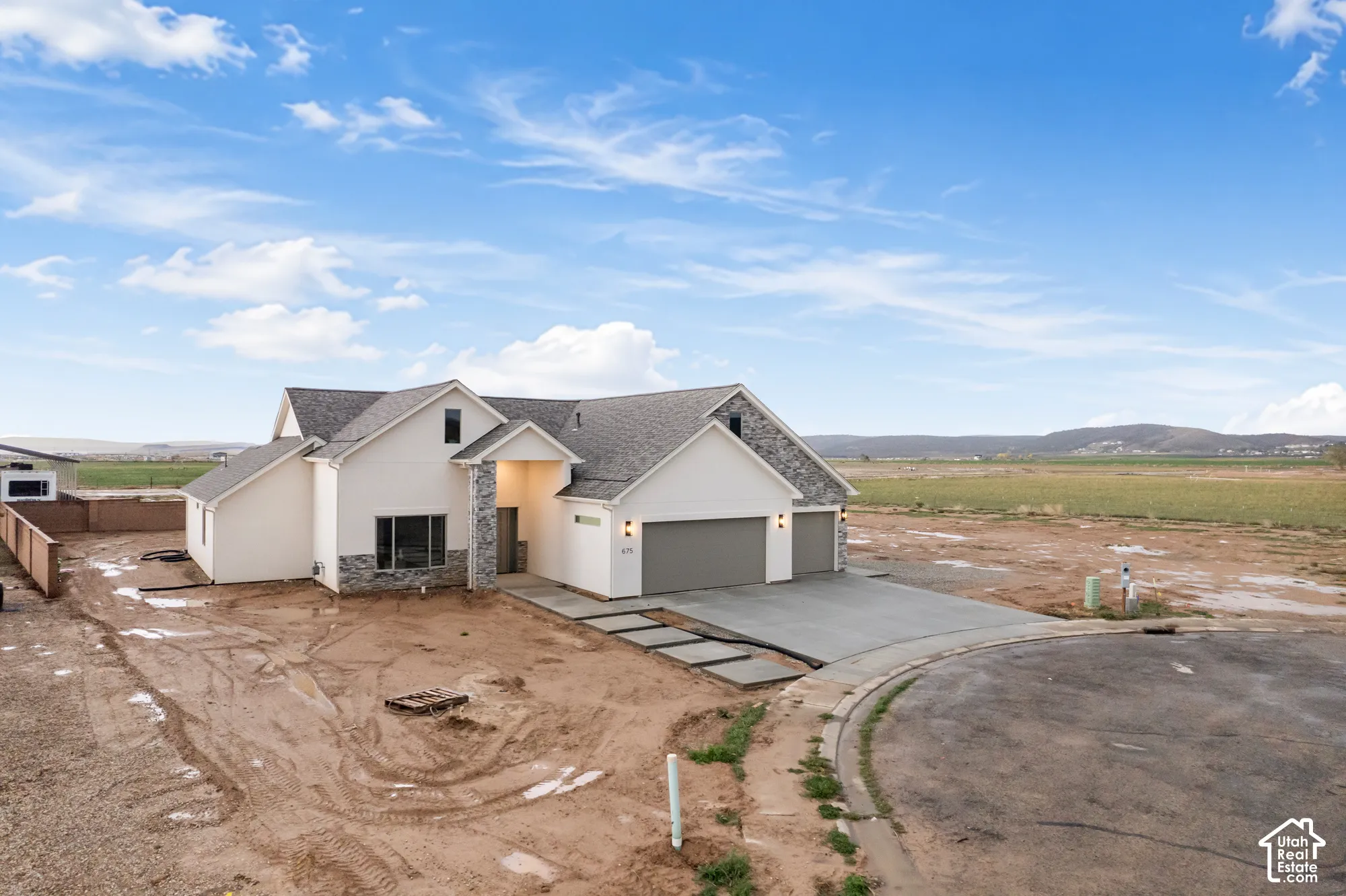 Modern residence featuring a multi-gabled roofline, stone veneer accents, light-toned siding, a multi-car garage, and a paved concrete walkway