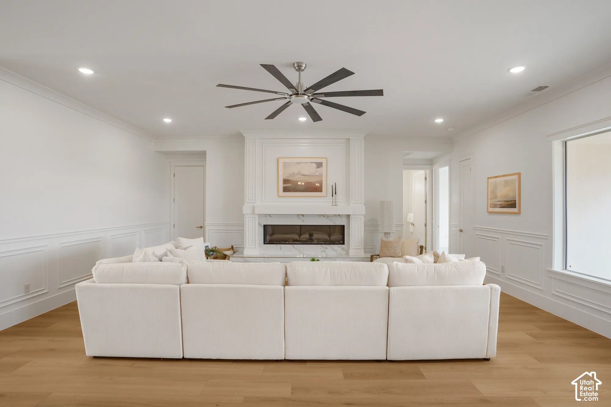 Fireplace with a stone-surround mantel, wood-finish flooring, recessed lighting, multi-blade ceiling fan, and wainscoting