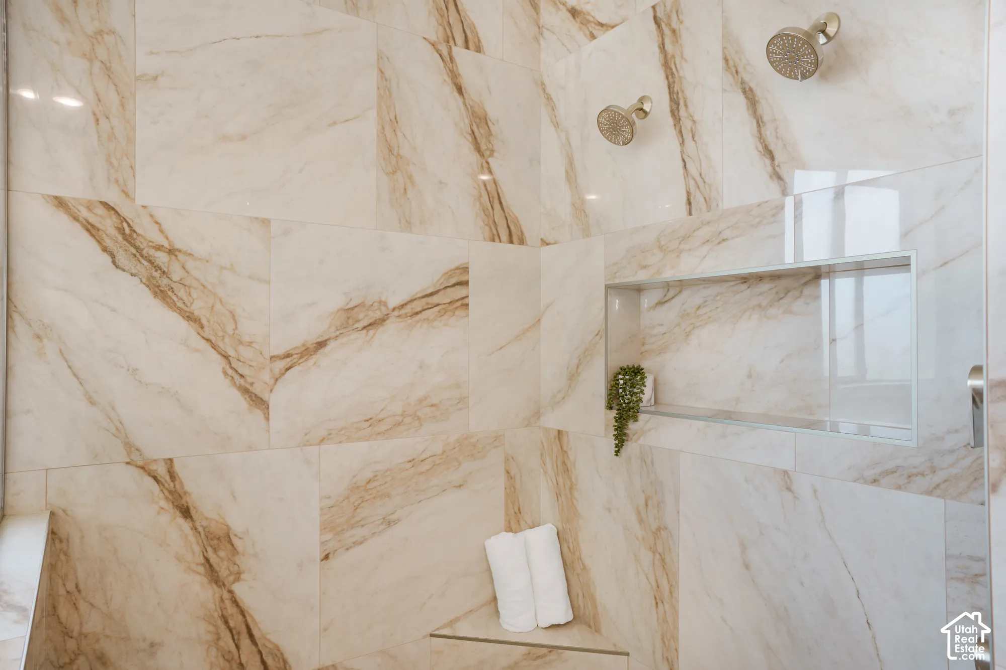 Walk-in shower featuring large-format stone-patterned wall tile, dual rainfall shower heads, a built-in recessed niche, and a triangular corner bench
