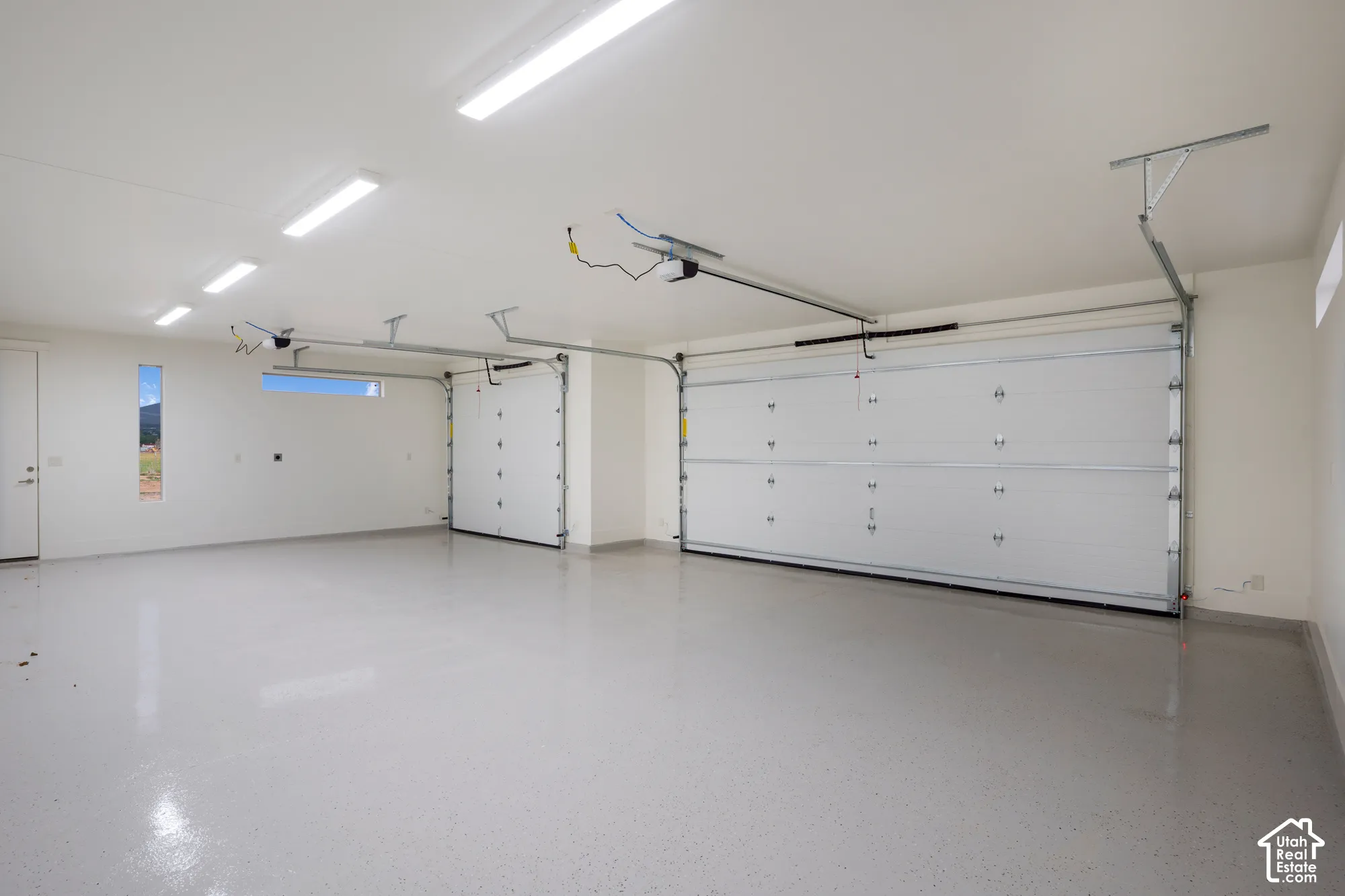 Spacious multi-car garage featuring finished epoxy flooring, high-intensity overhead LED lighting, and two individual sectional garage doors