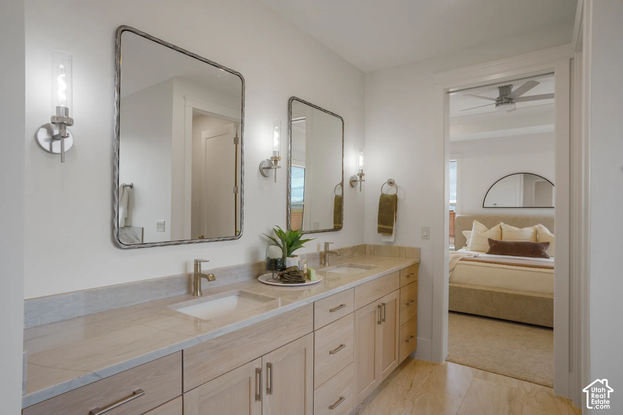 Double vanity featuring light wood cabinetry, stone countertops with integrated rectangular sinks, polished metallic fixtures, and dual wall-mounted mirrors