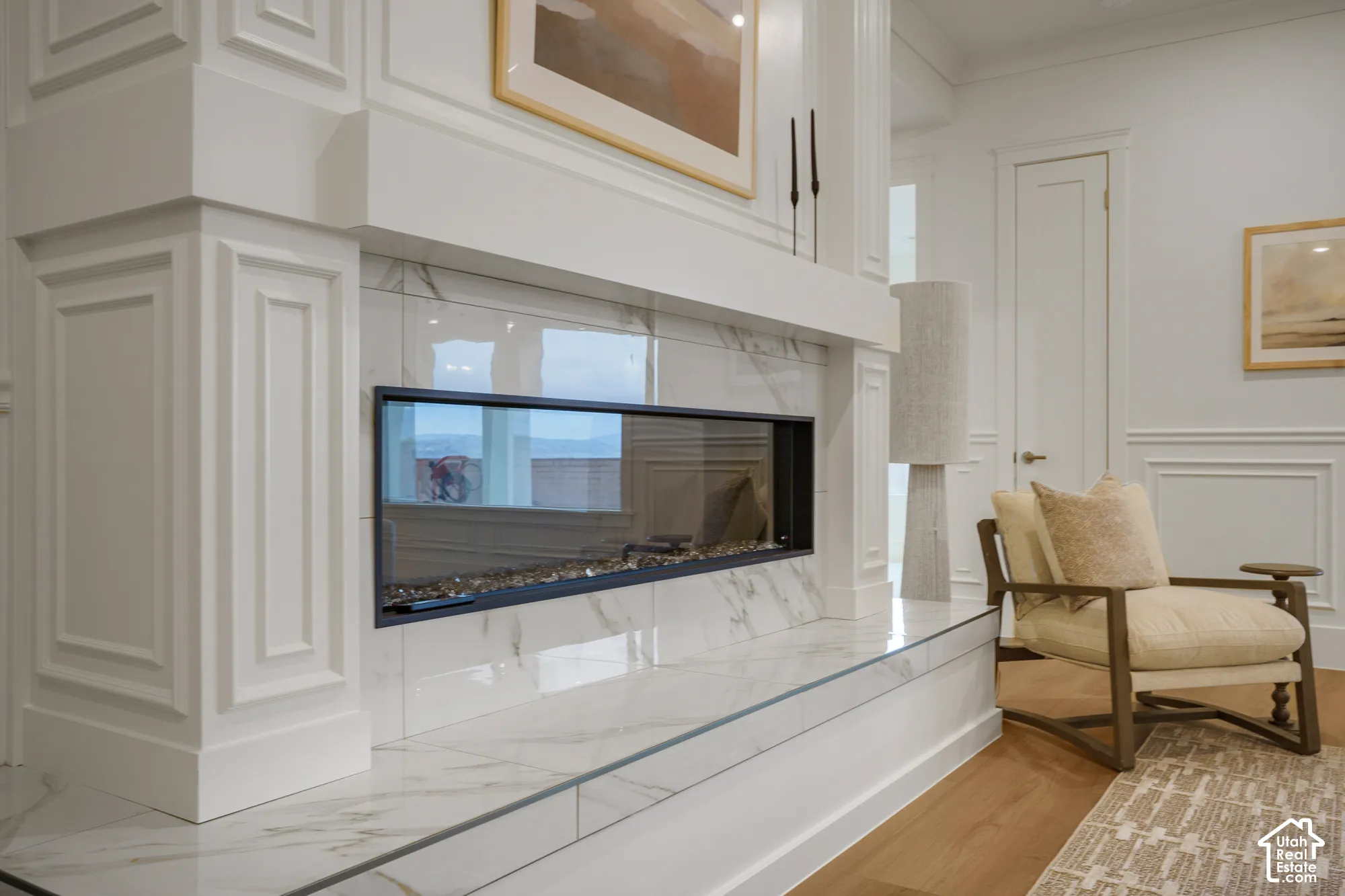 Linear gas fireplace featuring a stone-finish surround, extensive millwork, a wide hearth, and wood-finish flooring