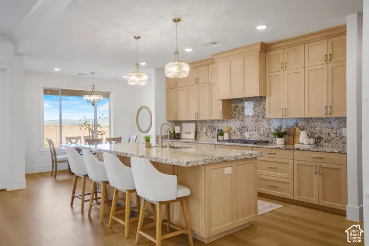 Kitchen featuring light-finish wood cabinetry, stone countertops, central island, wood-finish flooring, and pendant lighting