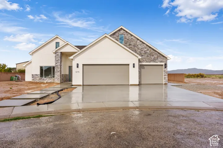Multi-gabled exterior with stucco finish and stacked stone accents, three-car garage, and concrete paver walkway