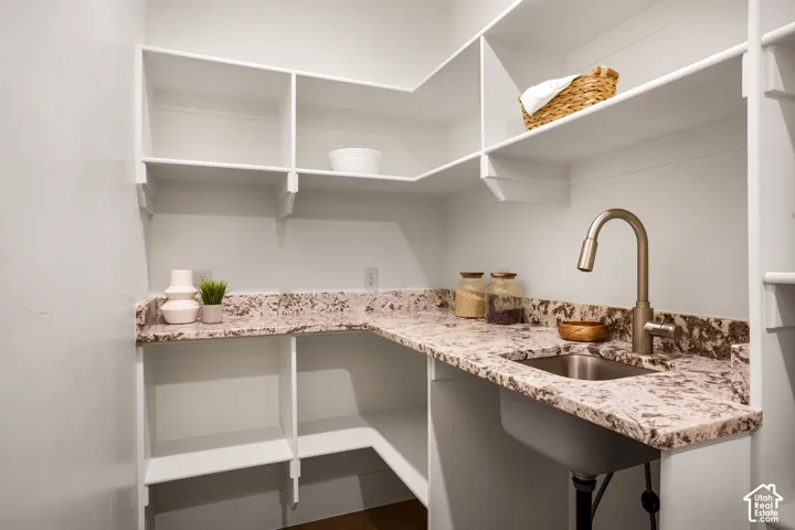 Walk-in pantry featuring white custom built-in shelving, speckled stone-finish countertops, an integrated stainless steel basin, and a high-arch gooseneck faucet