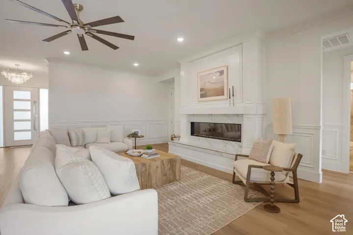 Linear fireplace with stone surround, custom millwork mantle, wood-finish flooring, wainscoting, and multi-blade ceiling fan
