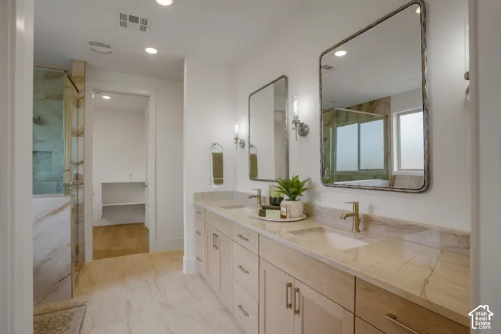 Dual-vanity cabinetry with neutral stone countertops, undermount sinks, wall-mounted light fixtures, framed mirrors, and stone-tile flooring