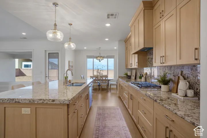 Kitchen featuring light-finish cabinetry, stone countertops, a large center island with a built-in sink, stainless steel gas cooktop, and pendant lighting