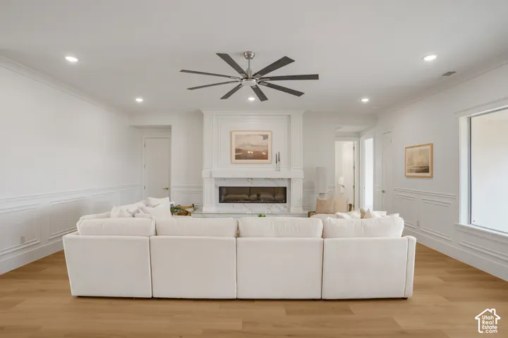 Fireplace with a stone-surround mantel, wood-finish flooring, recessed lighting, multi-blade ceiling fan, and wainscoting