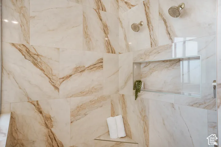 Walk-in shower featuring large-format stone-patterned wall tile, dual rainfall shower heads, a built-in recessed niche, and a triangular corner bench