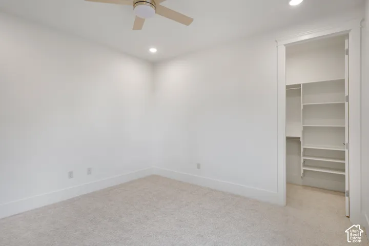 Neutral-toned carpeting, ceiling fan with integrated lighting, recessed lighting, and a walk-in closet featuring built-in shelving