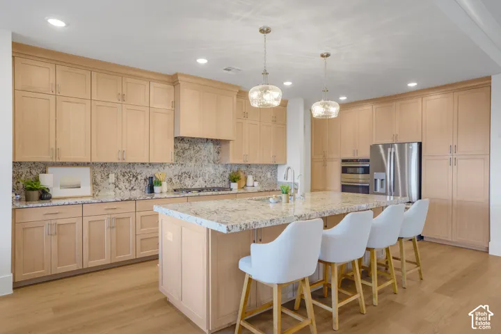 Kitchen featuring light-finish cabinetry, stone countertops, central island, stainless steel appliances, and dual glass pendant light fixtures