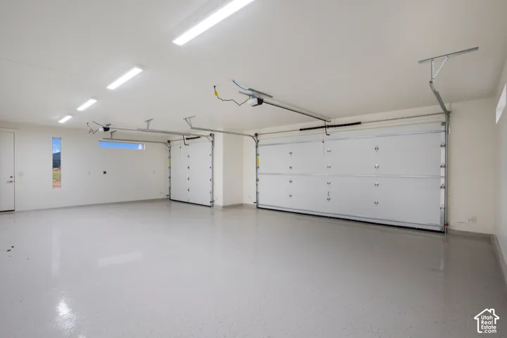 Spacious multi-car garage featuring finished epoxy flooring, high-intensity overhead LED lighting, and two individual sectional garage doors