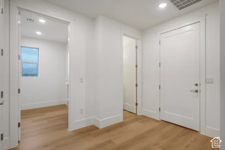 Interior hallway featuring wood-finish flooring, recessed lighting, solid-core doors, and crisp white trim