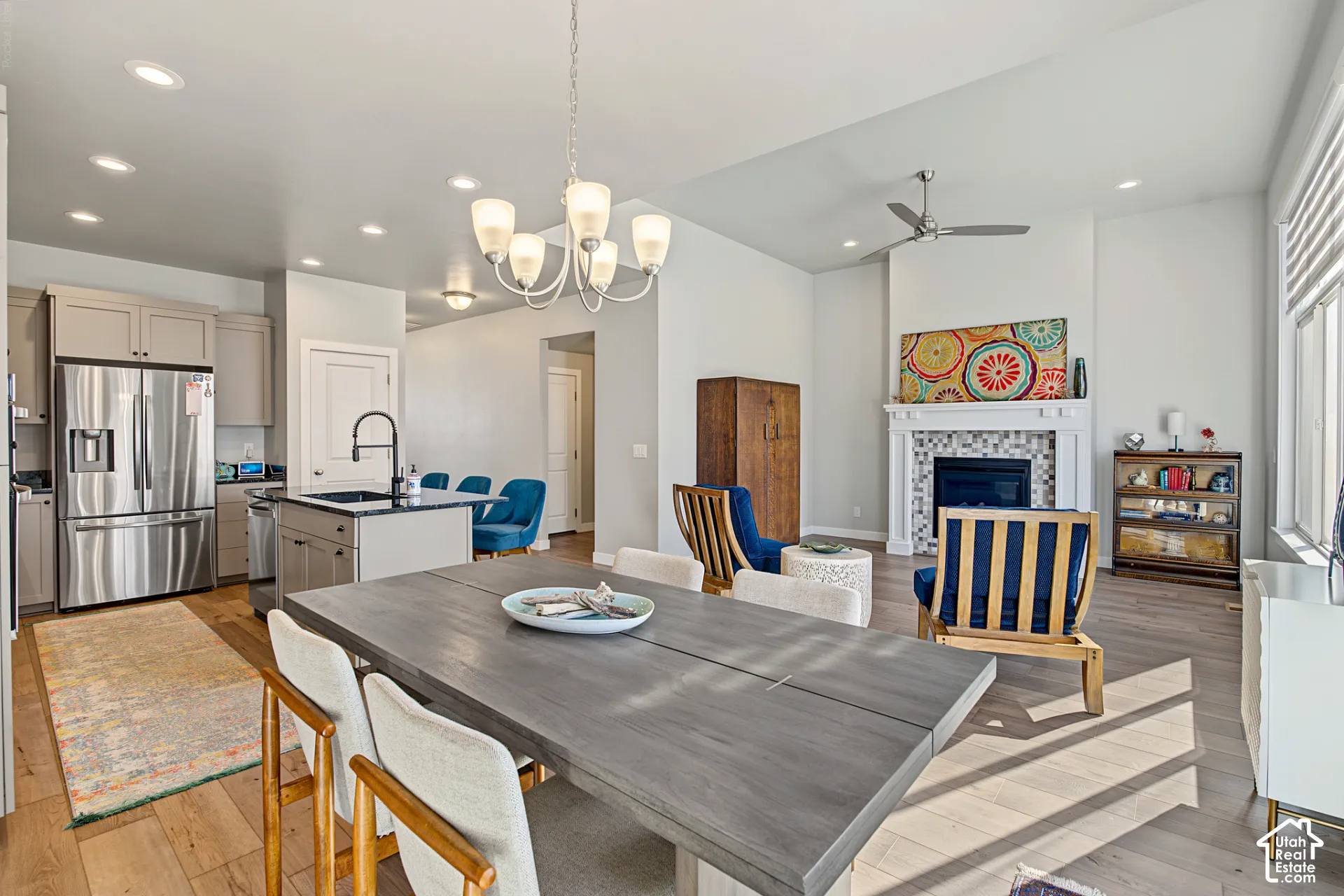 Open-concept kitchen and living area featuring recessed lighting, stainless steel appliances, wood-finish flooring, a kitchen island with stone surfacing, and a fireplace with a mosaic tile surround