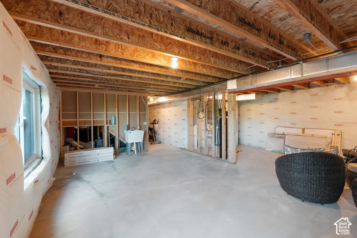Unfinished lower level featuring exposed wood joist ceilings, concrete flooring, insulated wall paneling, and an installed utility sink