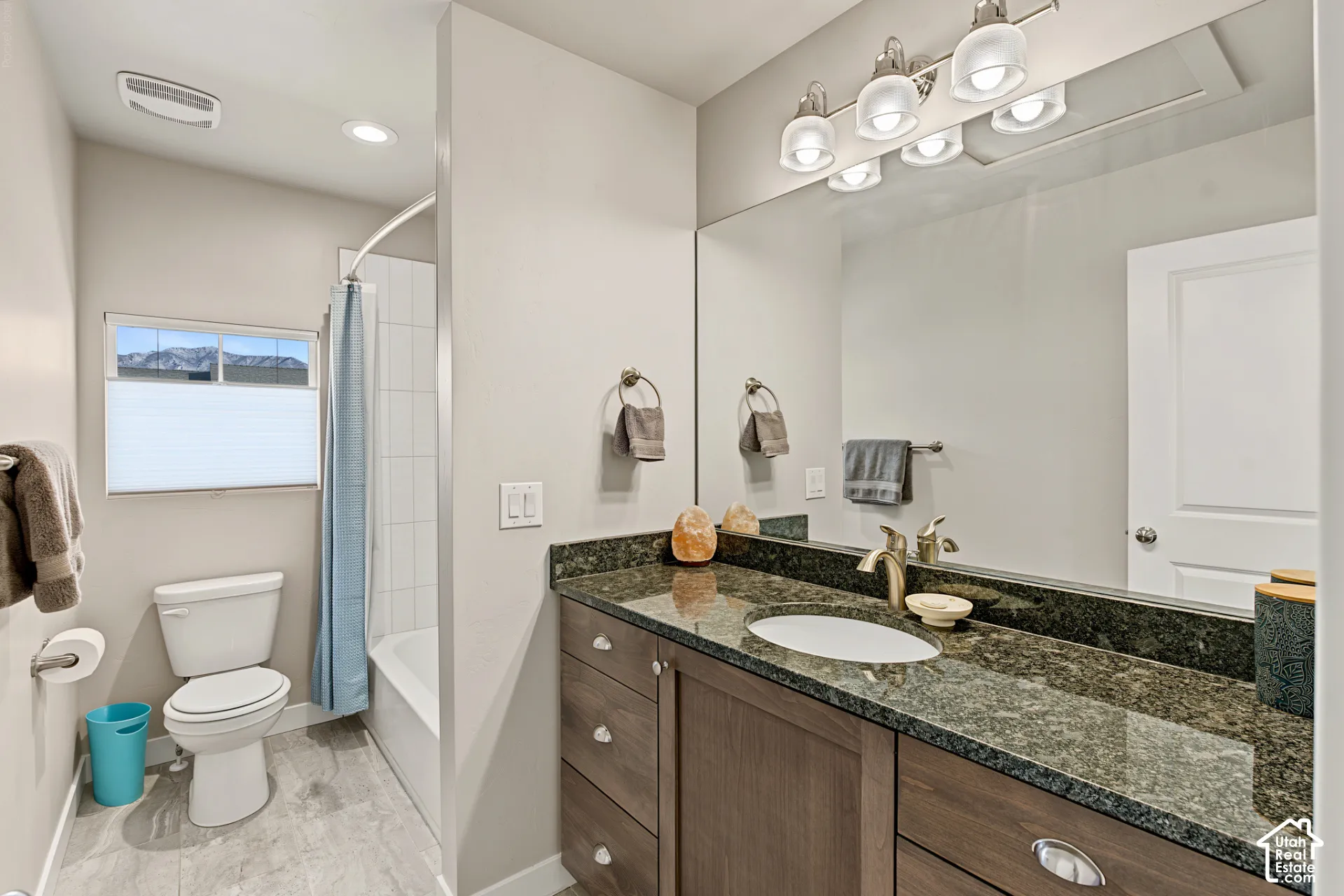 Bathroom featuring a vanity with dark-toned cabinetry, an integrated oval sink, and a stone-surface countertop, complemented by a large wall-mounted mirror, multi-bulb overhead lighting, and a bathtub with tile surround
