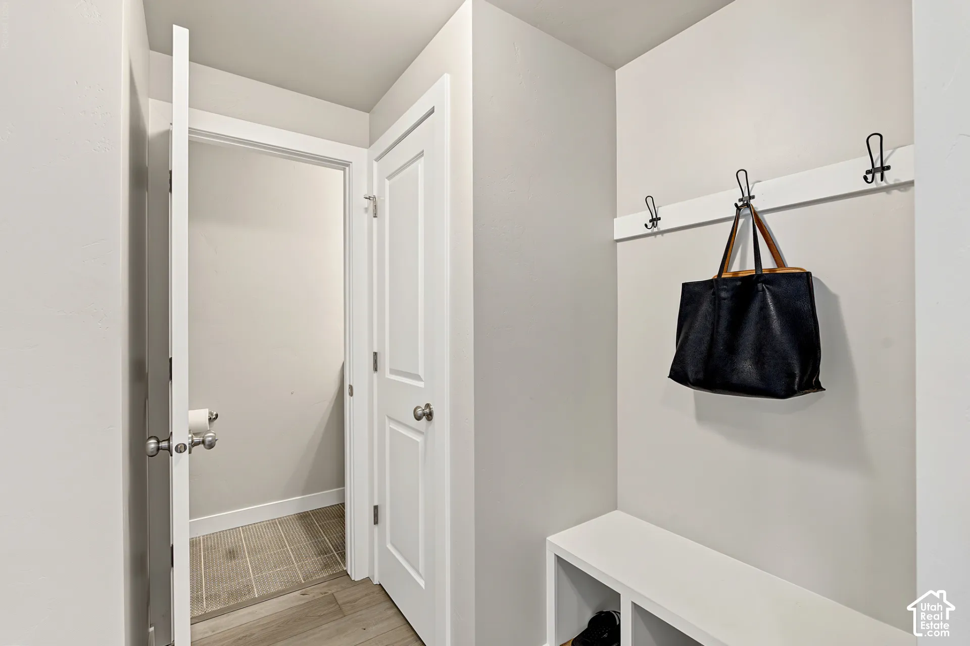 Built-in storage bench with lower shelving, mounted coat hooks, two-panel interior doors, and neutral wall tones