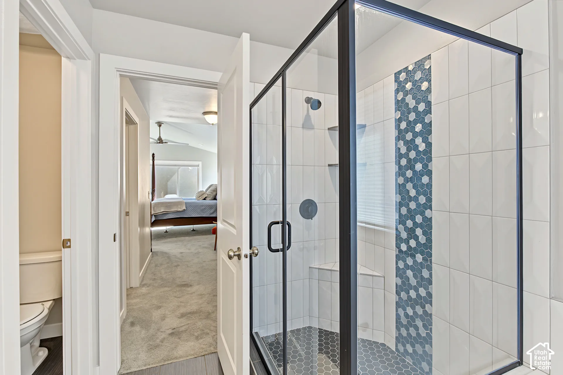 Walk-in shower featuring a glass enclosure with matte black framing, geometric mosaic tile accent wall, built-in corner shelving, and hexagonal tile flooring