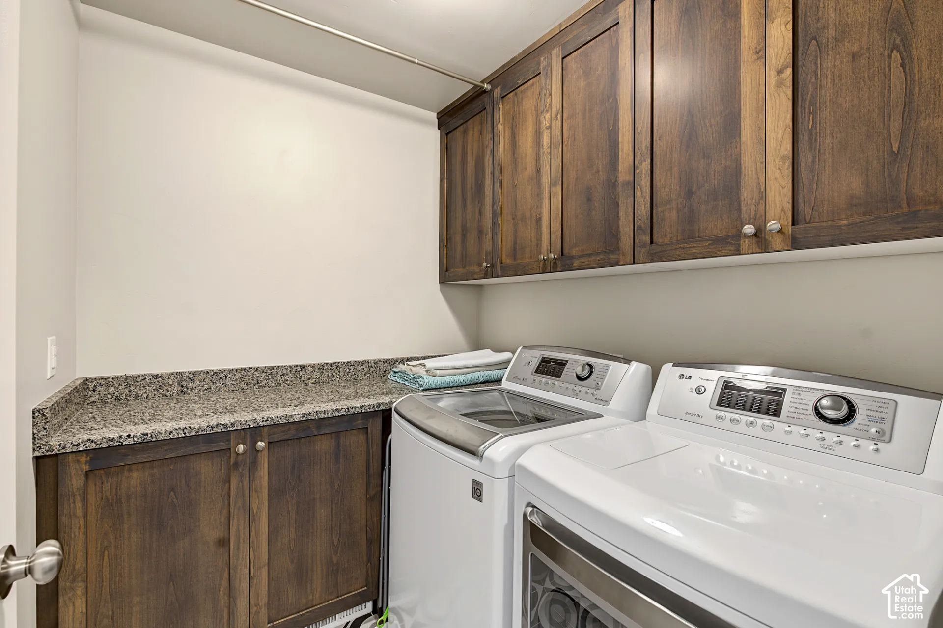 Laundry area featuring custom dark wood cabinetry, integrated stone-surface countertop, and a built-in clothing rod