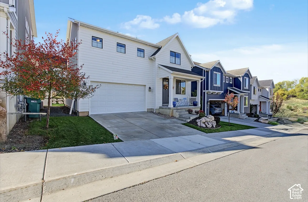 Two-story white horizontal siding exterior featuring a covered front porch, an attached two-car garage, concrete driveway, and landscape beds with stone accents
