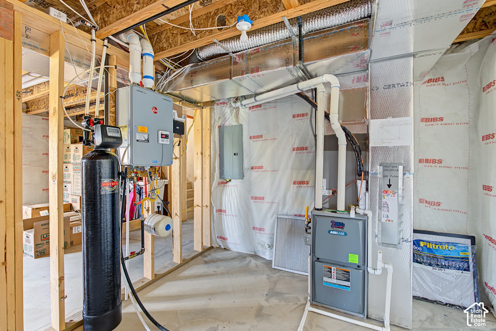 Mechanical area featuring a tankless water heater, high-efficiency furnace, water softening system, electrical service panel, and insulated wall barrier