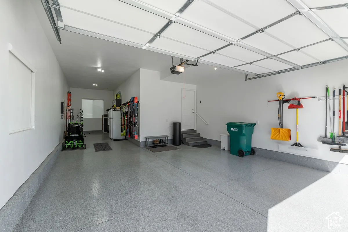 Attached garage featuring an epoxy-coated floor, overhead door, recessed lighting, and interior door with access steps
