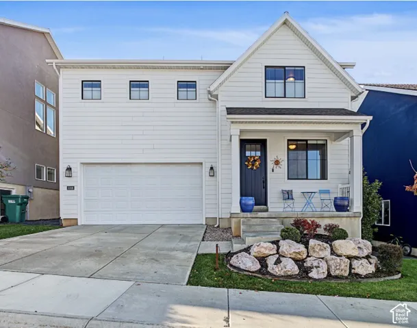 Two-story residence featuring white horizontal siding, a covered front porch, an attached garage, and stone landscaping accents