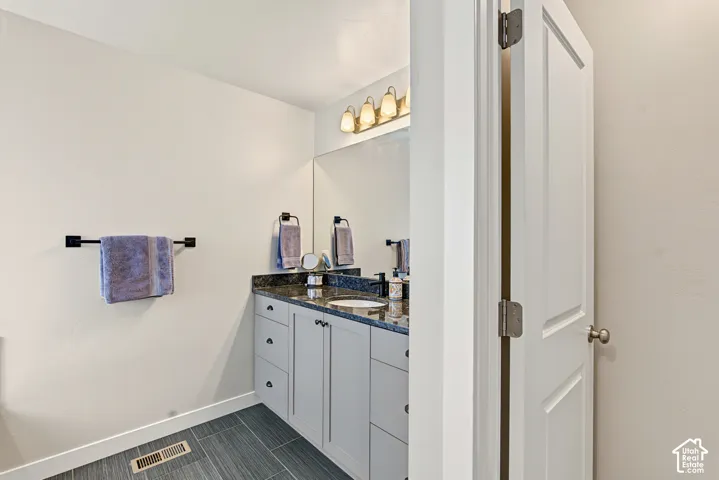 Bathroom featuring a gray vanity with stone-surfaced countertop, integrated sink, matte black hardware, large wall mirror, and porcelain tile flooring