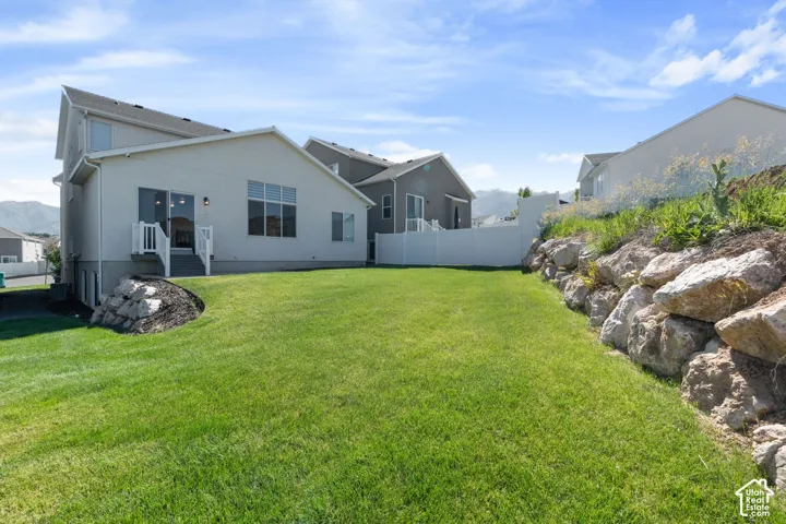 Backyard featuring a grass lawn, terraced boulder retaining wall, vinyl privacy fencing, and exterior staircase