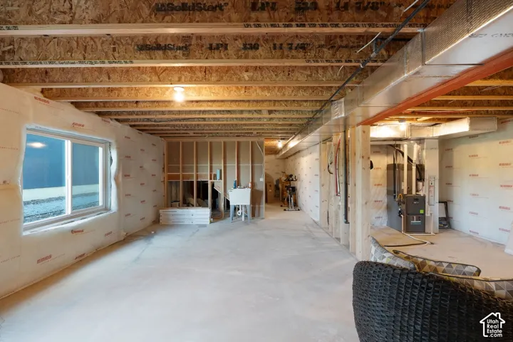 Unfinished interior space featuring exposed wood-joist ceiling, concrete flooring, dual-pane window, and installed utility furnace