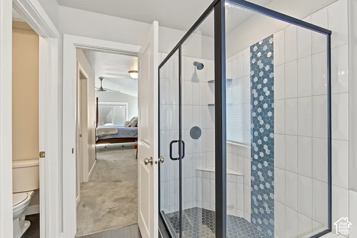Walk-in shower featuring a glass enclosure with matte black framing, geometric mosaic tile accent wall, built-in corner shelving, and hexagonal tile flooring