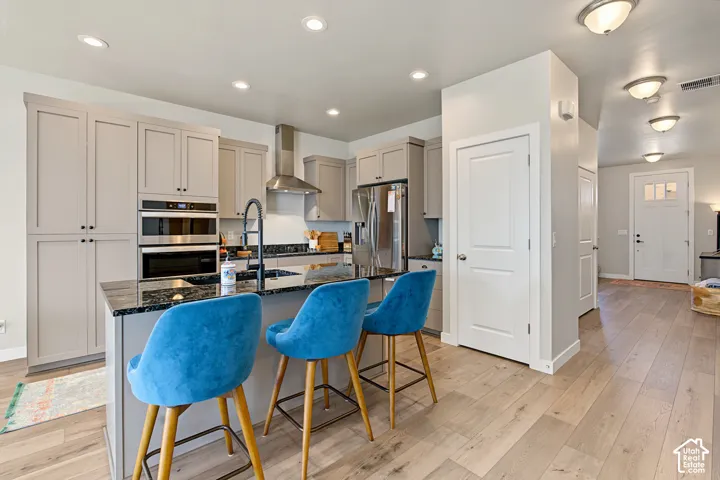 Kitchen featuring light-toned cabinetry, stone countertops, stainless steel appliances including a built-in wall oven and microwave, a kitchen island with a dark-finish faucet, and wood-finish flooring