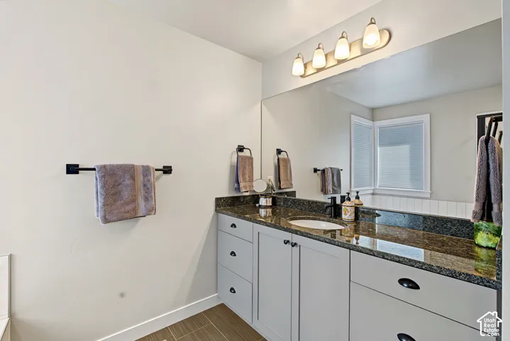 Vanity featuring light gray shaker-style cabinetry, dark stone countertop, integrated oval basin, matte black faucet, and full-width wall mirror