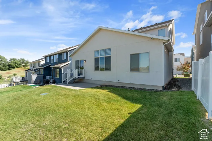 Rear exterior featuring a stucco facade, concrete patio, white vinyl privacy fencing, multi-pane windows, and a raised staircase with railings