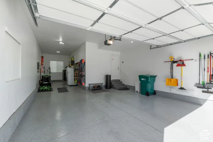 Attached garage featuring an epoxy-coated floor, overhead door, recessed lighting, and interior door with access steps
