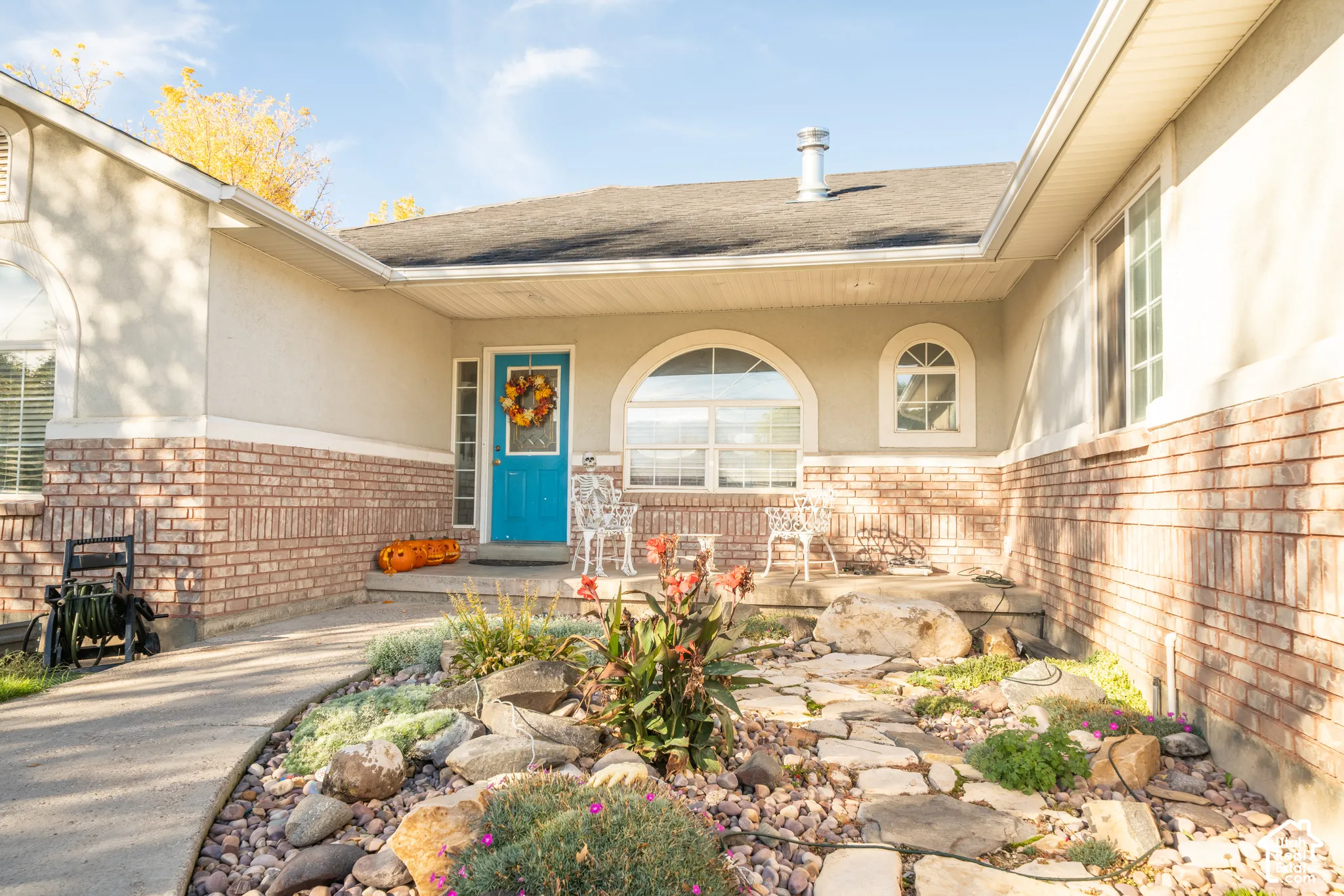 Exterior entry featuring a brick facade, covered concrete porch, arched window detailing, and xeriscaped front garden with natural stone path
