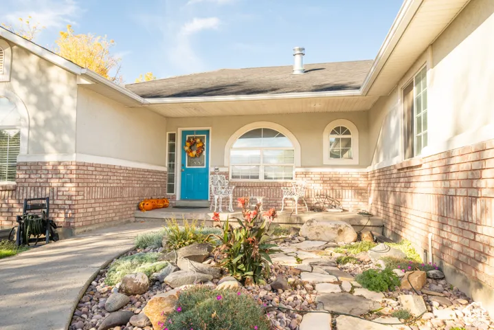 Exterior entry featuring a brick facade, covered concrete porch, arched window detailing, and xeriscaped front garden with natural stone path