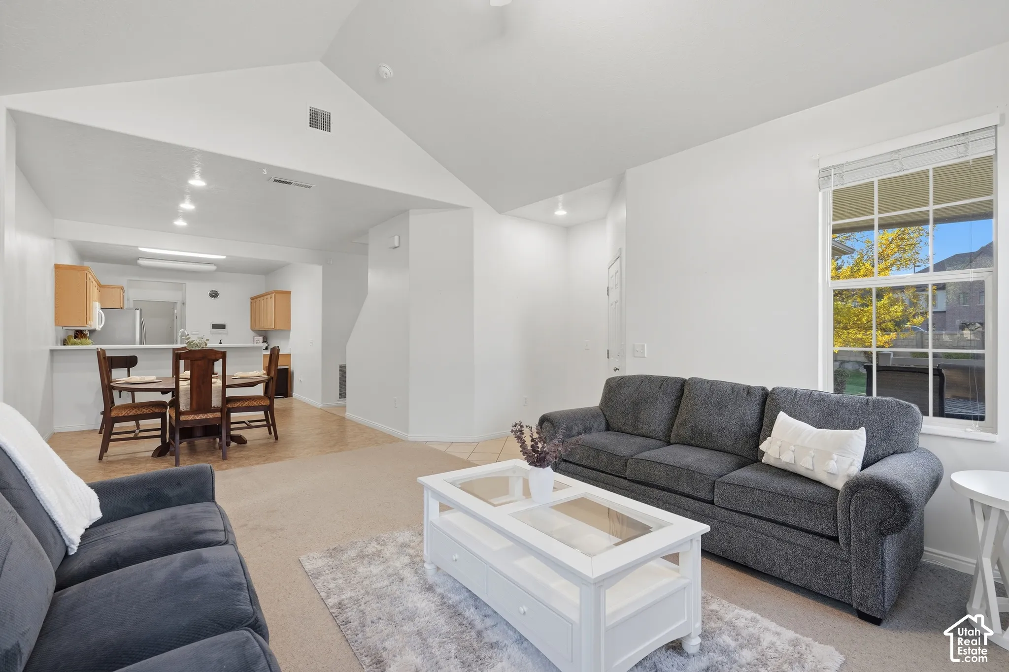 Vaulted ceilings, neutral wall palette, single-hung window with muntins, recessed lighting, and kitchen bar seating