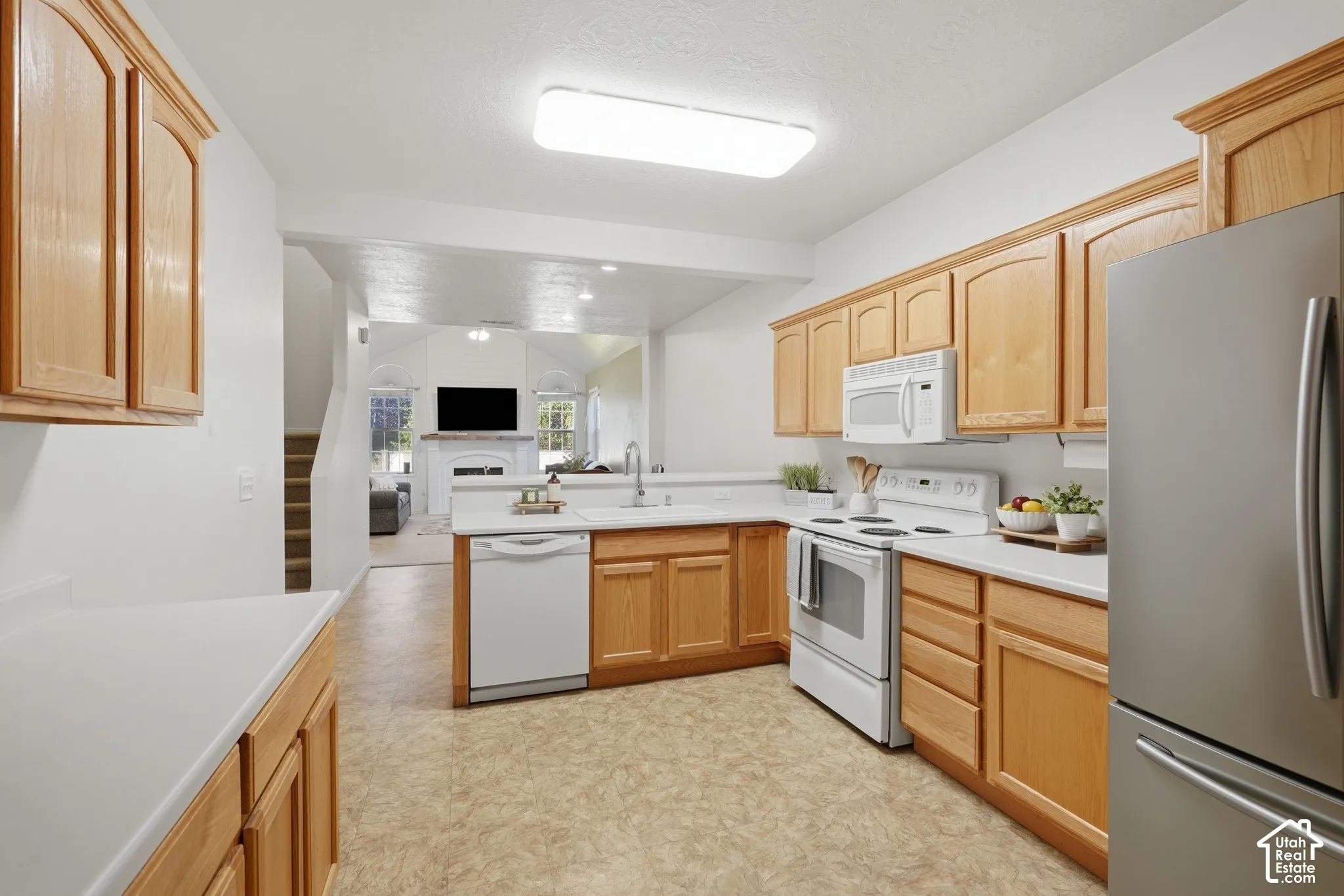 Kitchen featuring light wood cabinetry, white countertops, integrated white appliances, a stainless steel refrigerator, and resilient sheet flooring