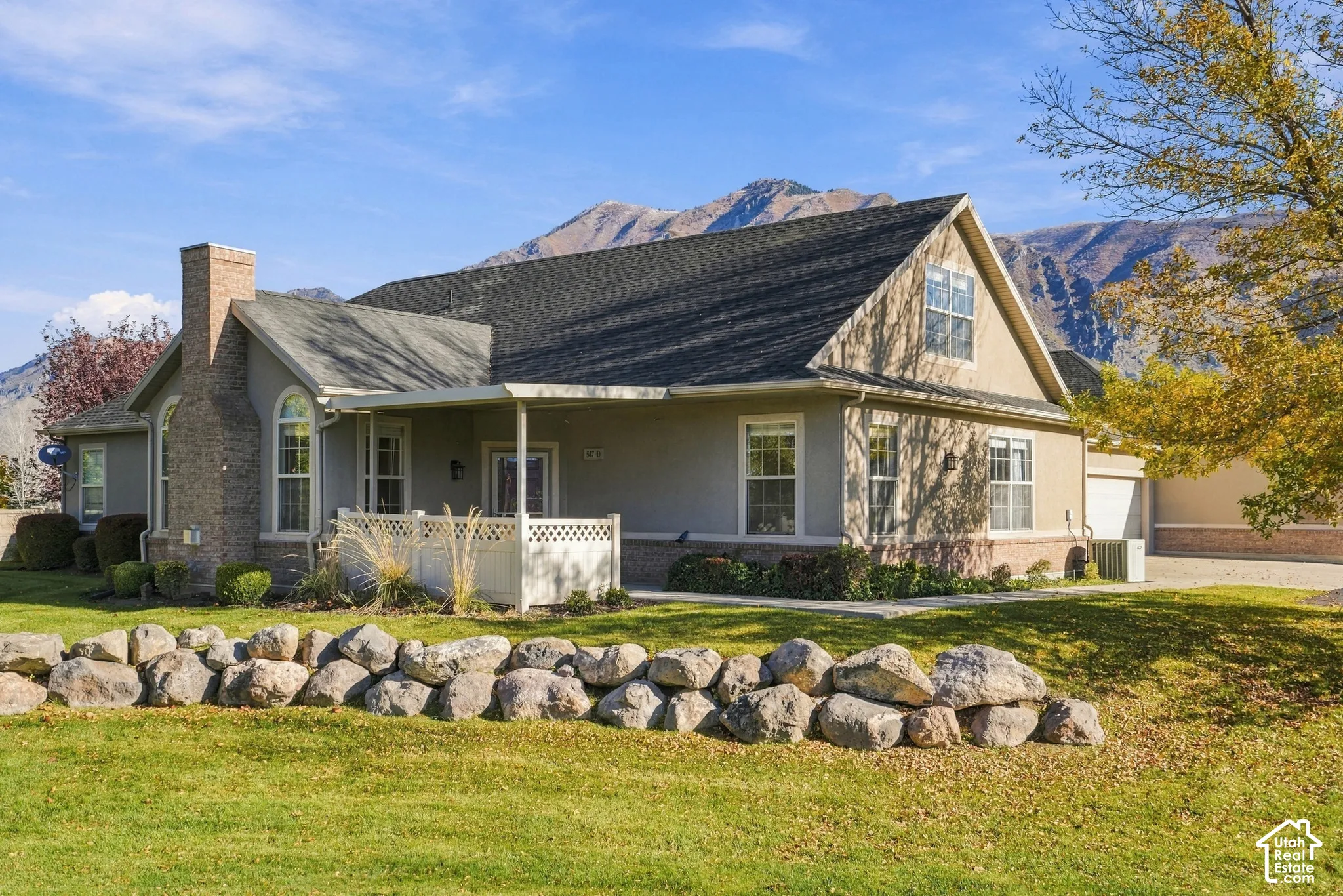 Exterior featuring a natural stone retaining wall, brick and stucco facade, covered porch with lattice railing, and a mountain backdrop