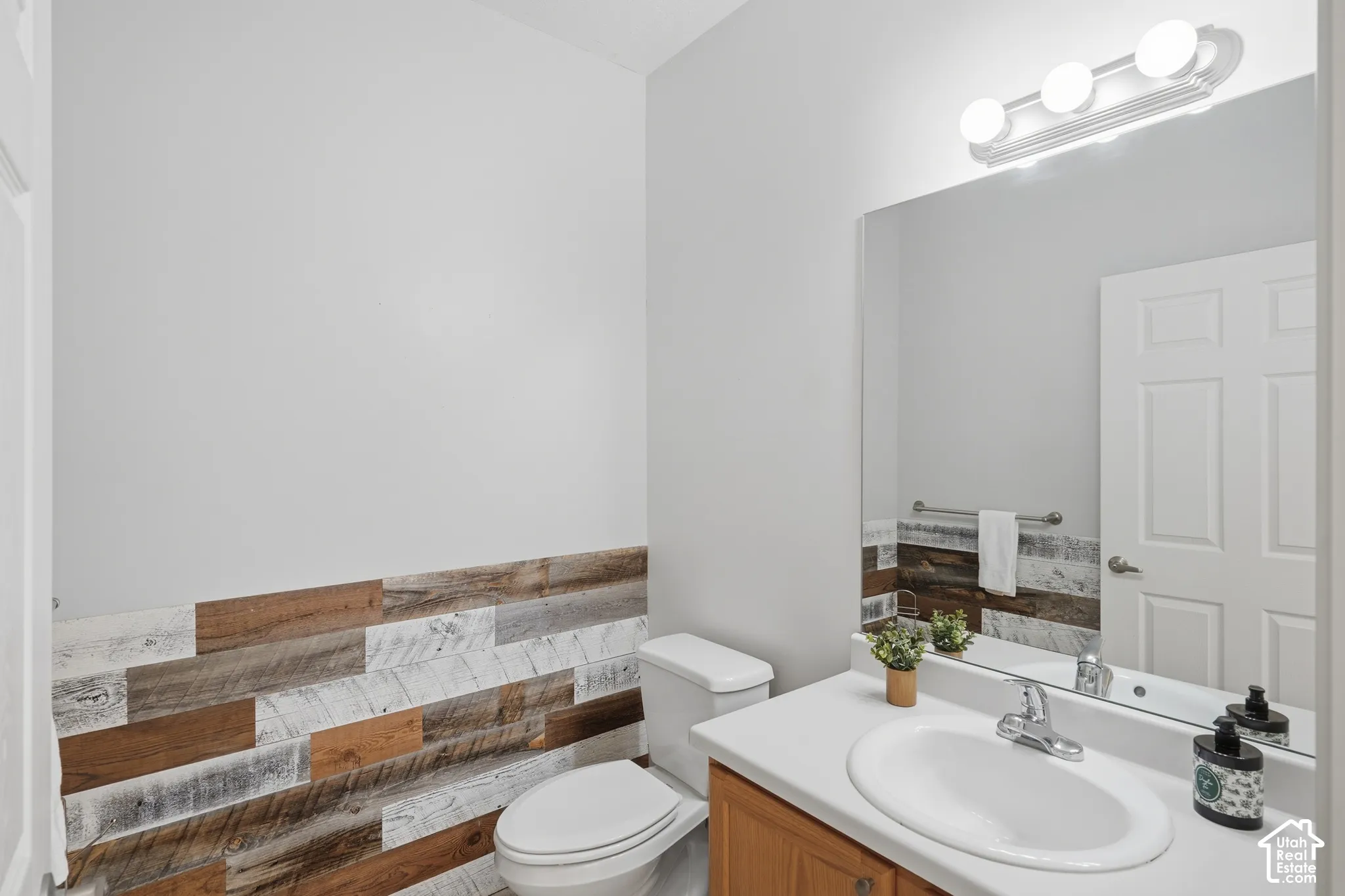 Bathroom featuring a wood-plank wainscoting, vanity with a solid-surface countertop, integrated oval sink, and a multi-bulb vanity light fixture